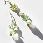Floral earrings with green leaves and white flowers on a light background