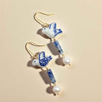 Earrings with ceramic dove charms and blue and white beads on a beige background