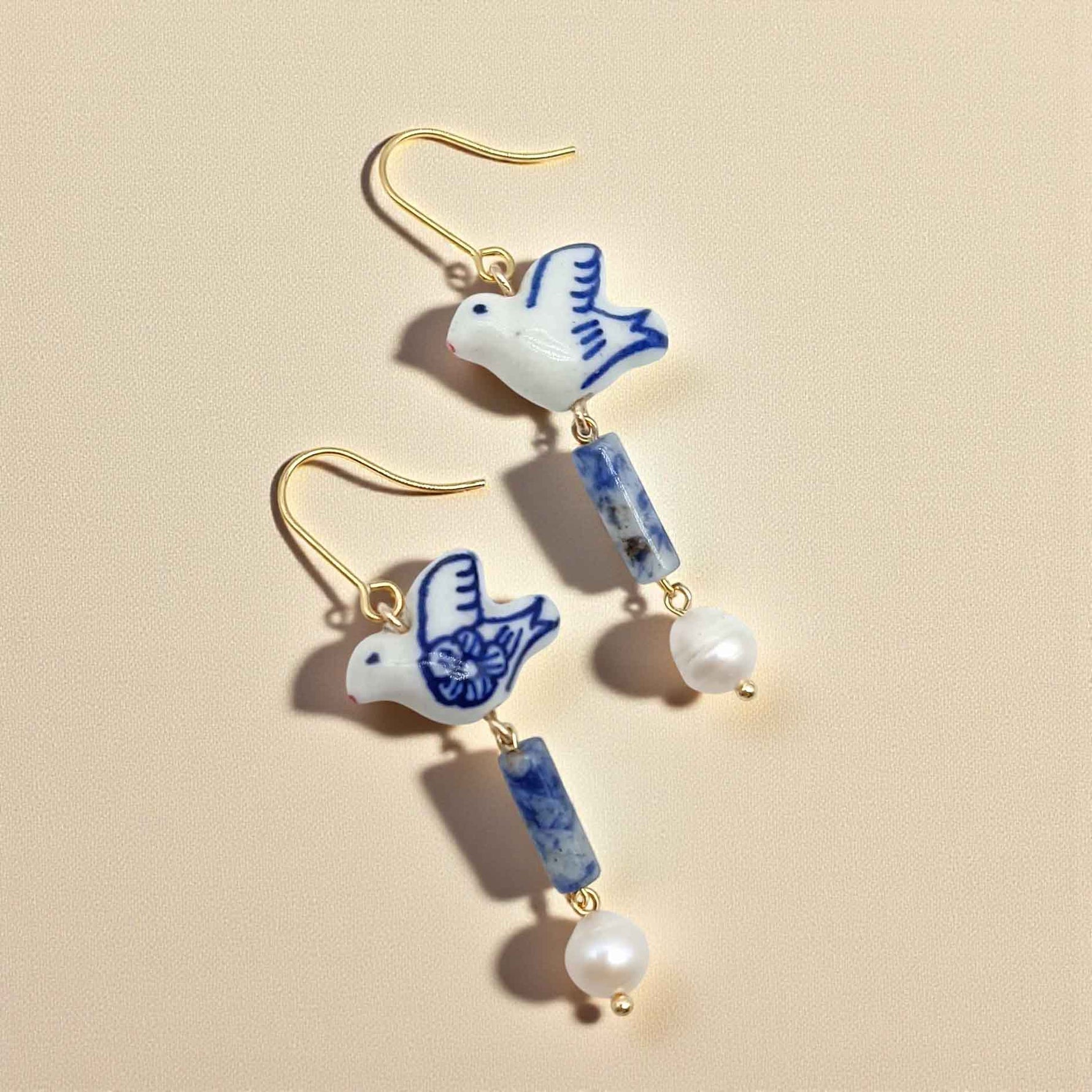 Earrings with ceramic dove charms and blue and white beads on a beige background