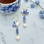 Ceramic dove earrings with blue and white design on a marble surface with a floral teacup.