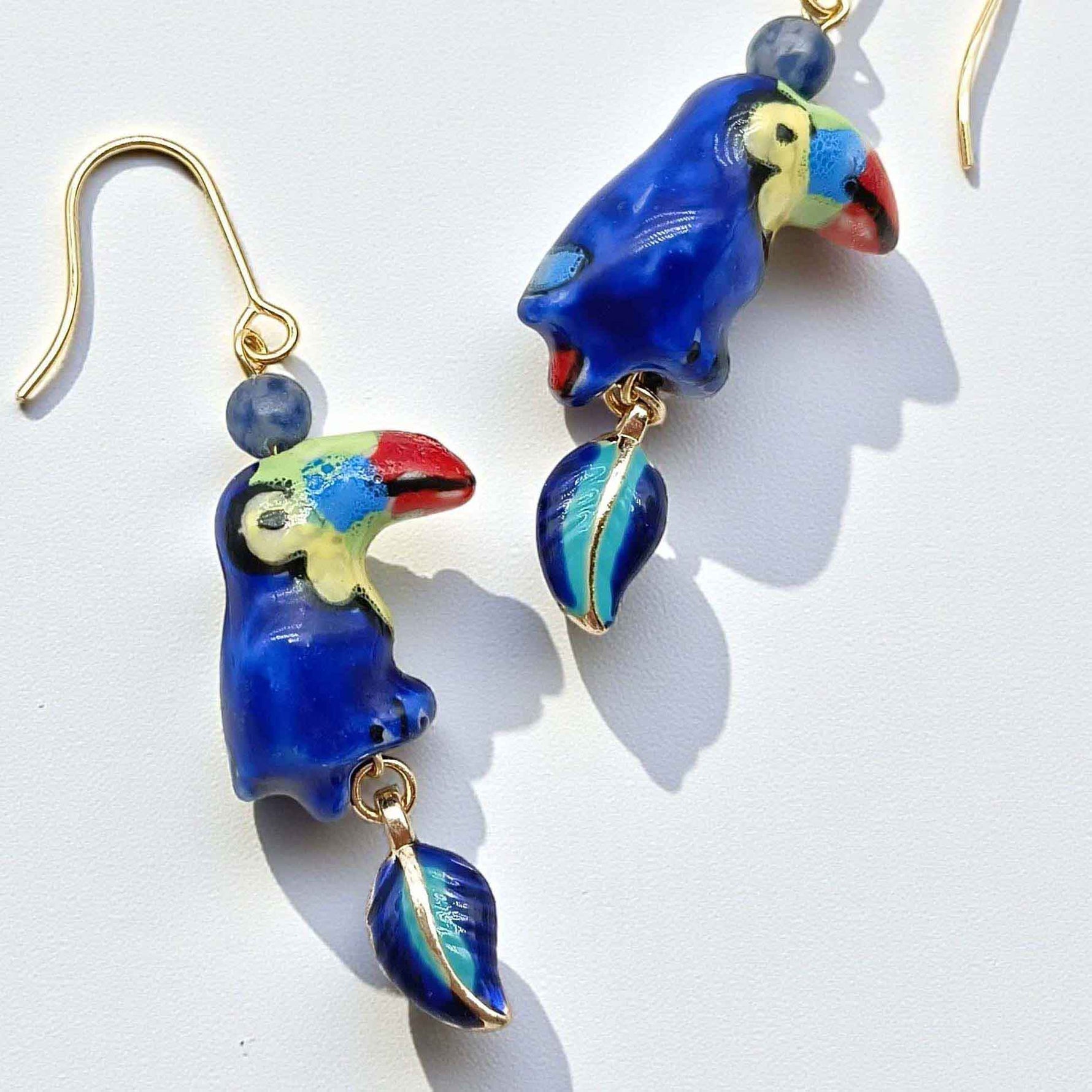 Parrot-shaped earrings with blue and gold details on a white background