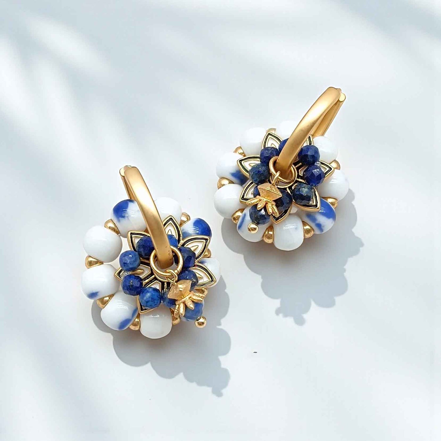 Pair of gold hoop earrings with blue and white stone accents on a light background
