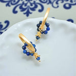 Gold hoop earrings with blue beads on a white dish with blue patterns