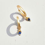Gold hoop earrings with blue gemstones on a white background