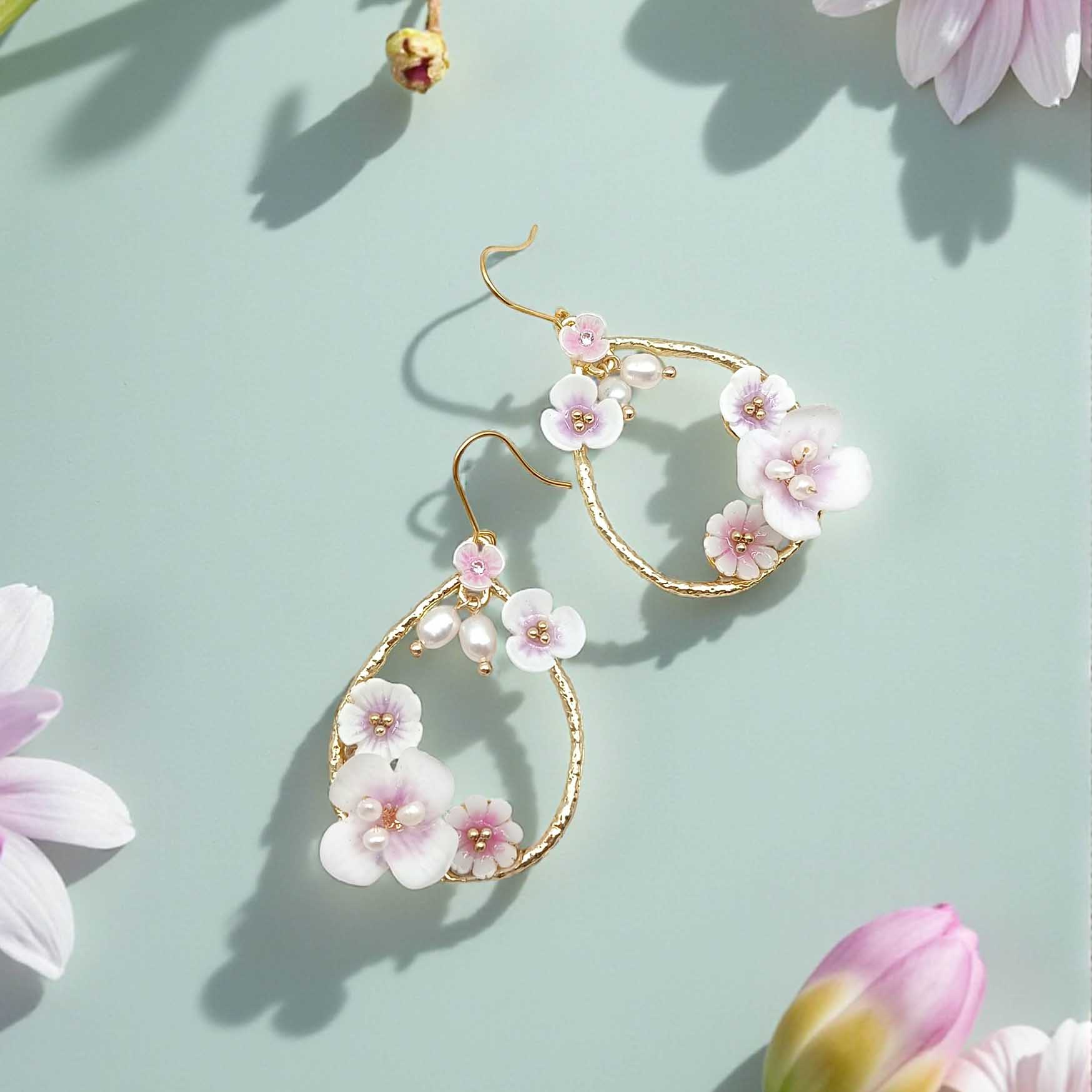Floral earrings with pink flowers and gold accents on a light green background with flowers.