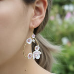 Gold teardrop earrings with pink and white enamel flowers and pearls, worn by model outdoors