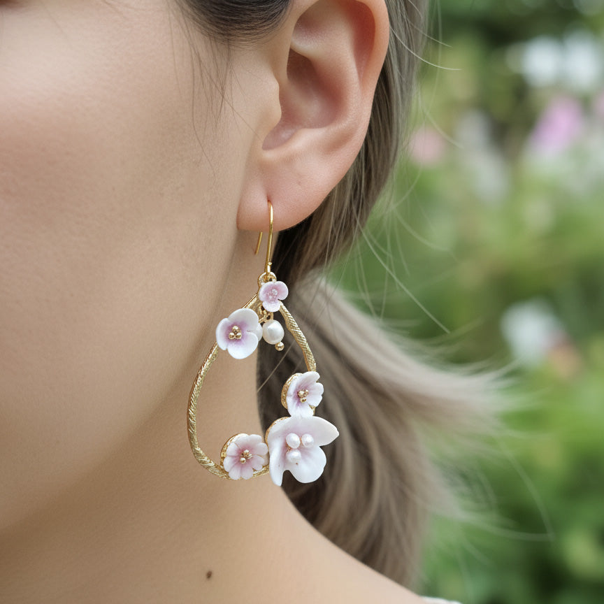 Gold teardrop earrings with pink and white enamel flowers and pearls, worn by model outdoors