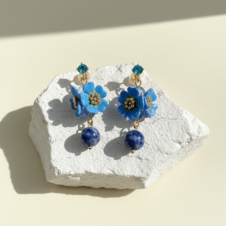 Blue floral drop earrings with gemstone accents displayed on stone base.