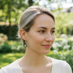 Model wearing pink resin floral earring with pearl drop in garden setting.