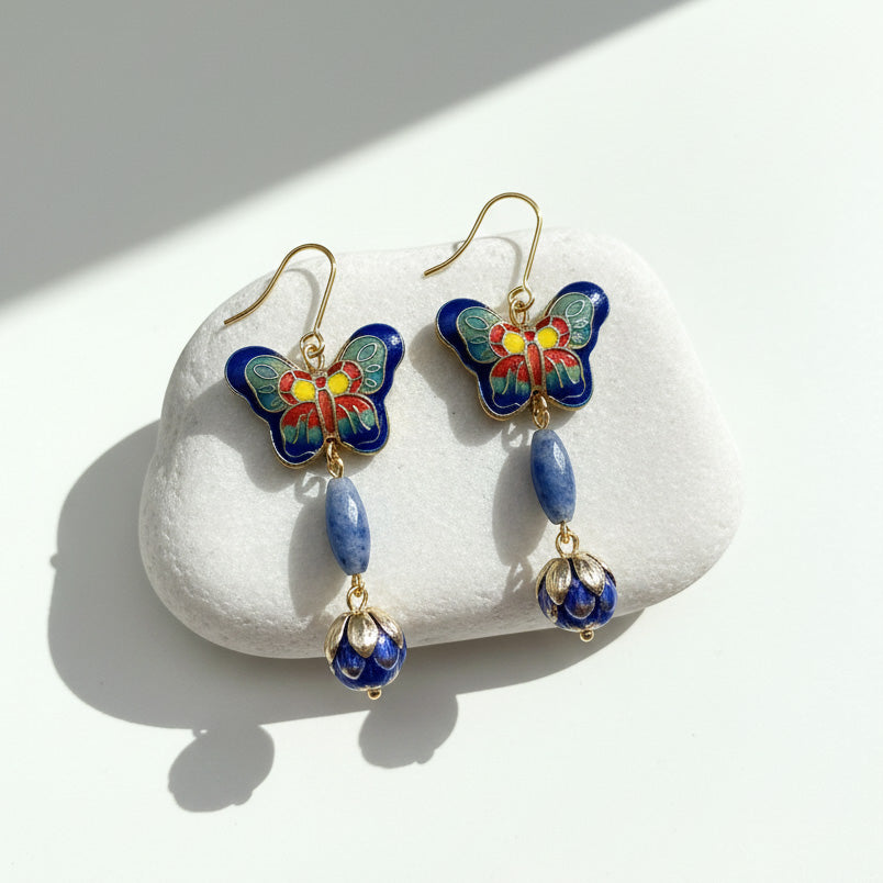 Cloisonné enamel butterfly and lapis drop earrings on white stone with sunlight and shadow.