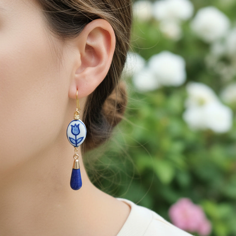 Close-up of an ear wearing a blue and white floral earring with a blurred floral background