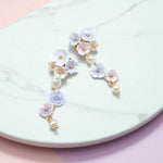 Flat lay of pastel floral and pearl earrings on marble background, delicate feminine jewelry.