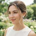 Model wearing A2K London hand-painted flower and pearl drop earrings in garden sunlight, elegant style.