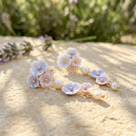 Floral earrings with pearls on a sandy surface with blurred lavender flowers in the background