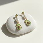 Avocado drop earrings with pearls displayed on white stone.