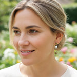 Model wearing avocado and pearl earrings in garden sunlight.