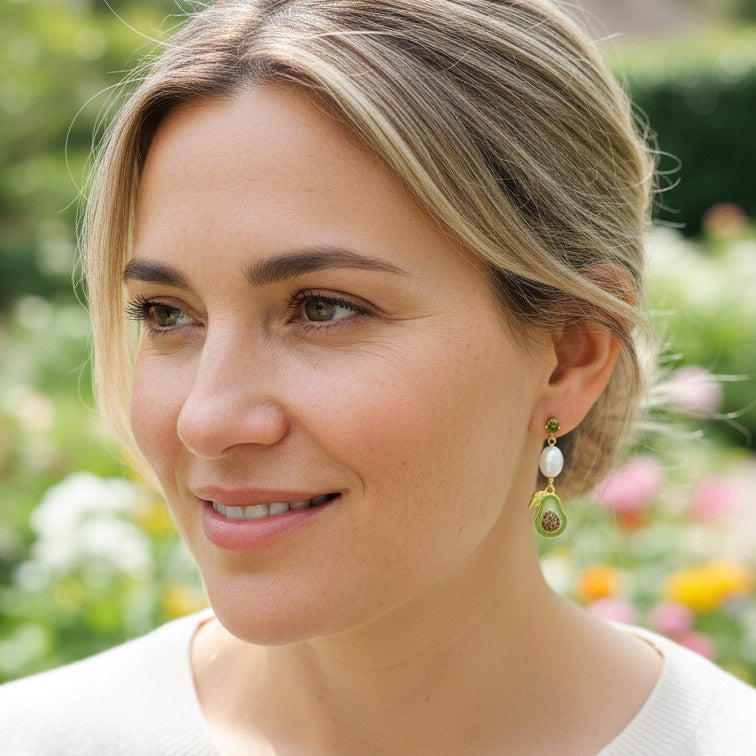 Model wearing avocado and pearl earrings in garden sunlight.