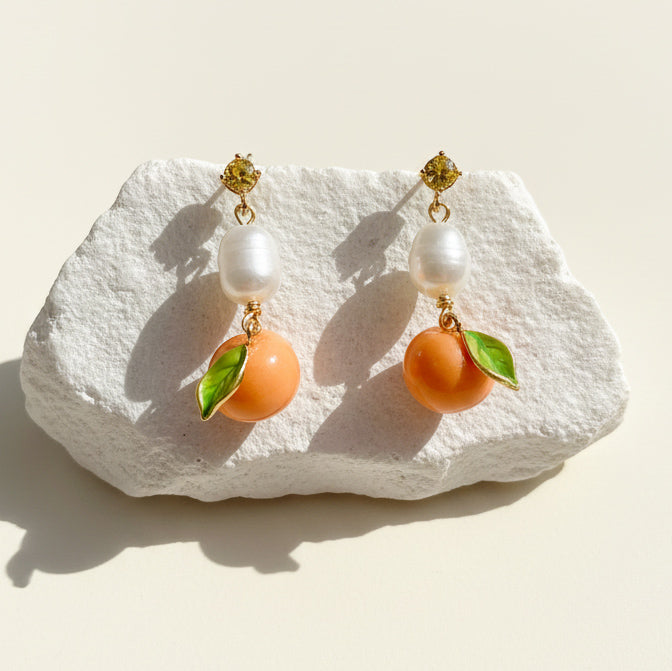 Hand-painted enamel mandarin and pearl drop earrings on white stone background, sunlight and shadow.