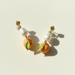 Side view of enamel mandarin drop earrings showing pearl and leaf detail, sunlight and shadow.