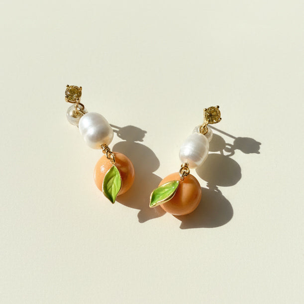 Side view of enamel mandarin drop earrings showing pearl and leaf detail, sunlight and shadow.