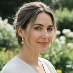 Model wearing A2K London mandarin and pearl drop earrings in garden sunlight, elegant playful style.