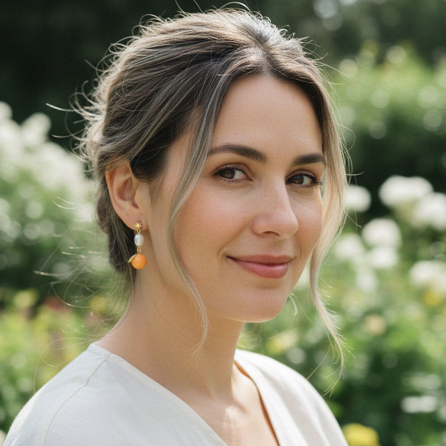 Model wearing A2K London mandarin and pearl drop earrings in garden sunlight, elegant playful style.