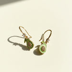 Hand-painted avocado hook earrings on cream background with sunlight and shadow.