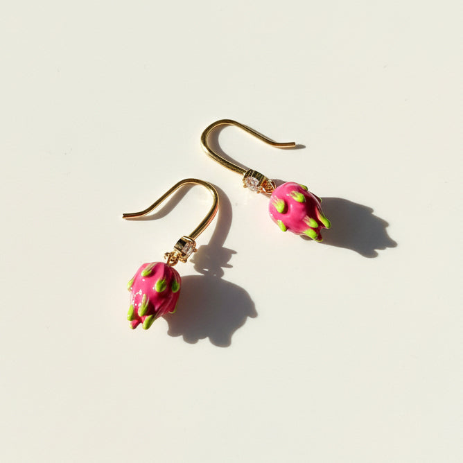 Hand-painted dragon fruit hook earrings on cream background with sunlight and shadow.