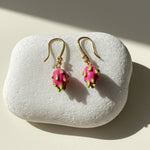 Close-up of enamel dragon fruit earrings with CZ stone on white stone background.