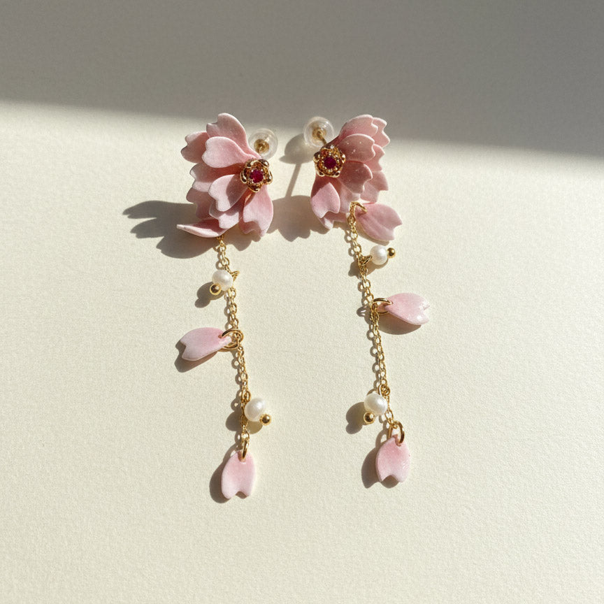 Pair of pink floral earrings with gold chains on a light background
