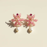 Pink spider lily flower earrings with pearl drops on a beige background
