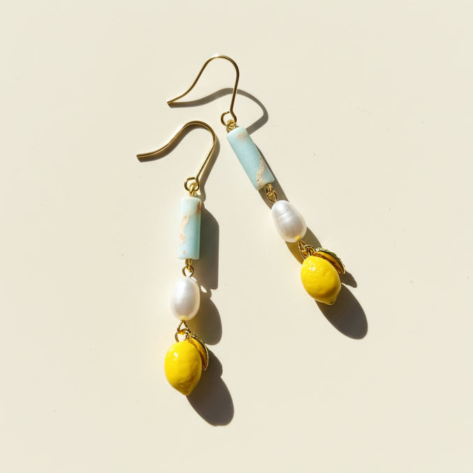 Hand-painted lemon and pearl drop earrings with aqua stone on cream background, sunlight and shadow.