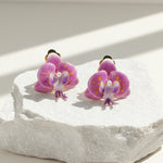 Hand-painted purple orchid resin clip-on earrings on stone display