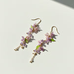 Hand-painted wisteria resin drop earrings with amethyst and pearls on white background.