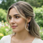 Model wearing hand-painted wisteria earrings in soft garden light.