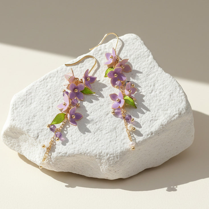 Purple and green wisteria floral drop earrings displayed on textured stone.