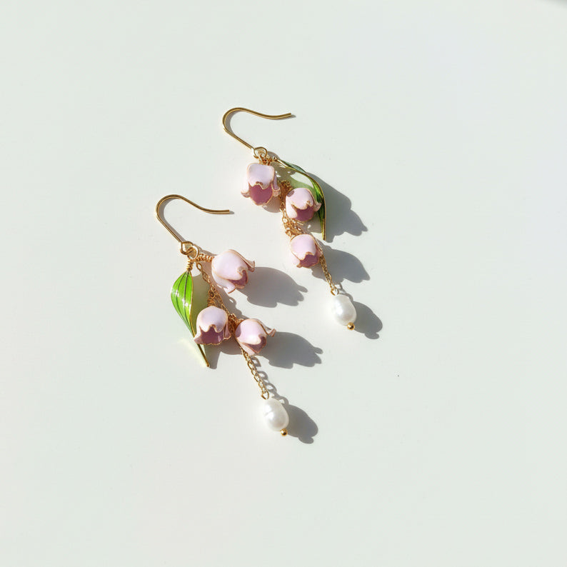 Pair of earrings with pink floral and pearl designs on a light background