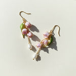 Pair of floral earrings with pink flowers and gold leaves on a light background