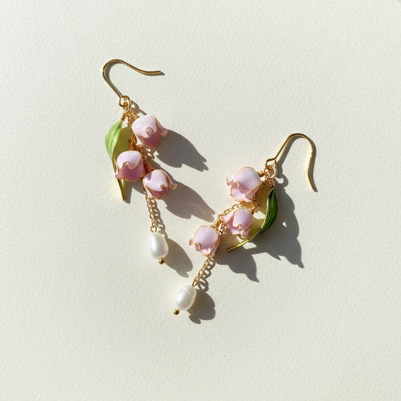 Pair of floral earrings with pink flowers and gold leaves on a light background