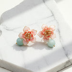 Pink lotus earrings with blue-green stone displayed on marble background.