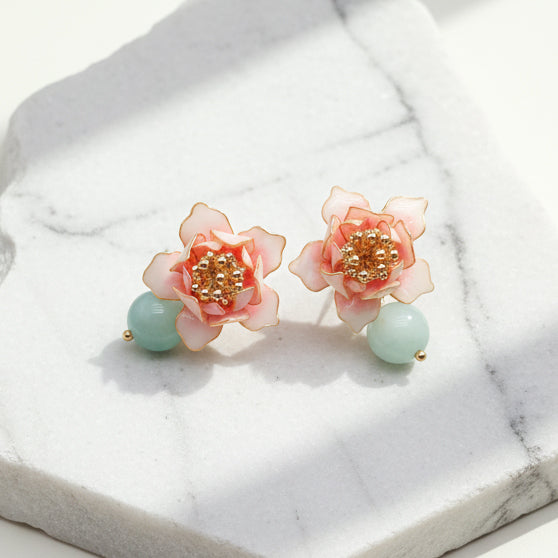Pink lotus earrings with blue-green stone displayed on marble background.