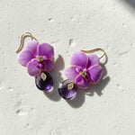 Purple flower-shaped earrings with gold accents on a light gray background