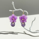 Purple orchid flower-shaped earrings with purple teardrop beads on a white branch against a gray background