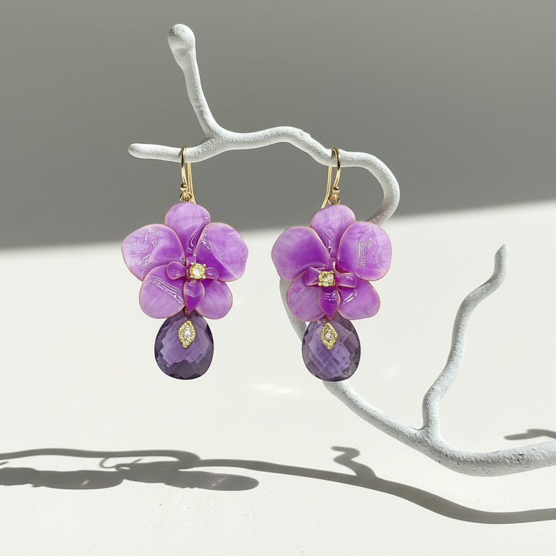 Purple orchid flower-shaped earrings with purple teardrop beads on a white branch against a gray background