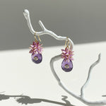 Artistic floral earrings hanging from branch in soft light.