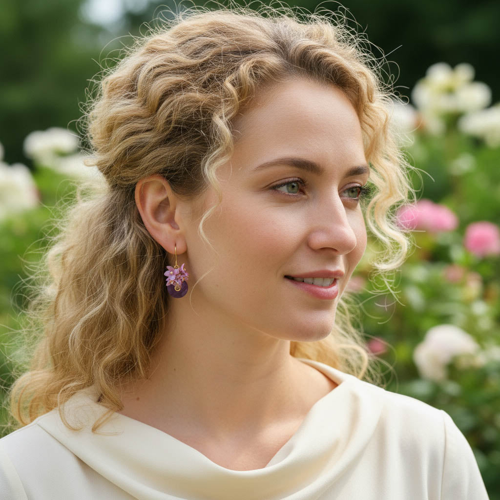 Model wearing pink floral and amethyst earrings in a garden.