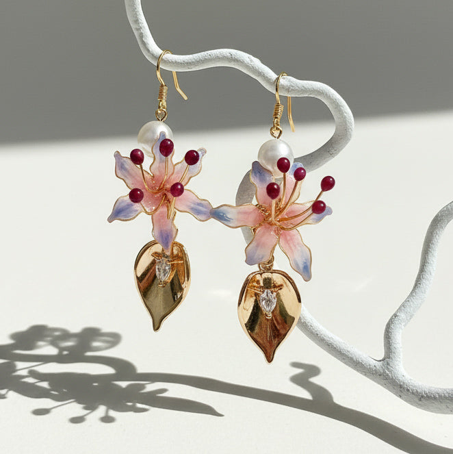 Hanging view of gold-plated pink lily floral earrings with pearl accents and CZ leaf details, sunlight and shadows.