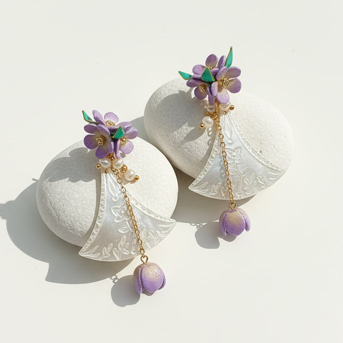 Hand-carved shell fan earrings with lilac flowers and pearl accents on white stones.