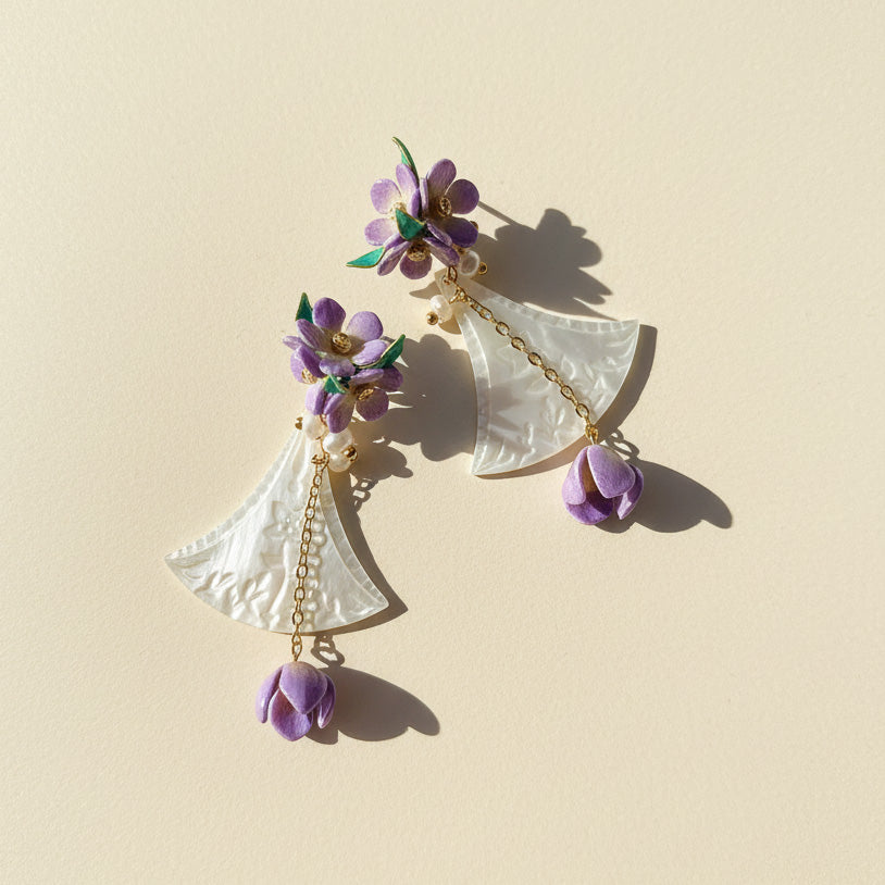 Shell fan earrings with gold chains and purple flower drops in sunlight.
