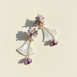 Iridescent shell and lilac flower earrings displayed on beige background.
